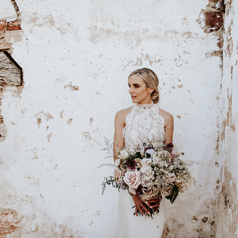 Bride holding a bouquet in front of a textured white wall.